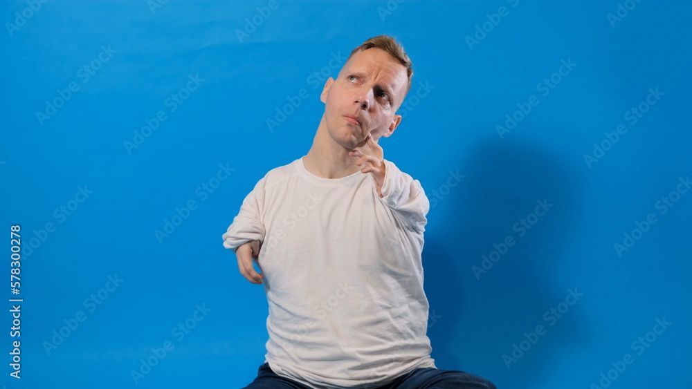 a man with disabilities of congenital pathology of the hands looks up thoughtfully sitting on an isolated blue background. a man with disabilities of congenital pathology of the hands looks up thoughtfully sitting on an isolated blue background.