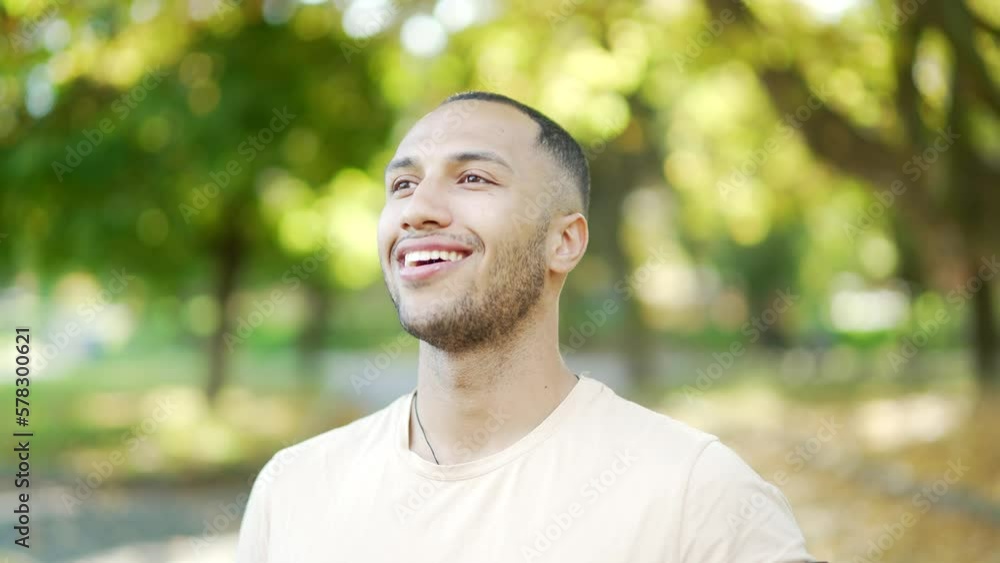Close up portrait of a young smiling man in a t-shirt standing and relaxing with closed eyes in an urban city park. Fit handsome mixed race male breathing deeply while looking away after a morning jog Close up portrait of a young smiling man in a t-shirt standing and relaxing with closed eyes in an urban city park. Fit handsome mixed race male breathing deeply while looking away after a morning jog