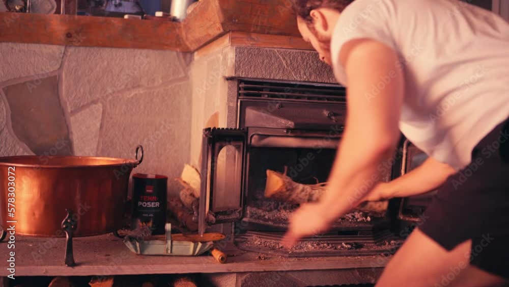Man In The House Opens Cast Iron Wood Burning Stove And Puts In Firewood. medium shot Man In The House Opens Cast Iron Wood Burning Stove And Puts In Firewood. medium shot