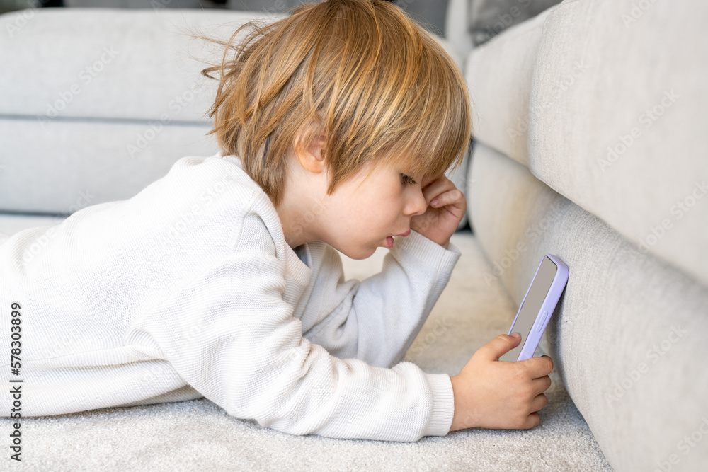 Adorable caucasian boy using smartphone sitting on sofa at home Adorable caucasian boy using smartphone sitting on sofa at home