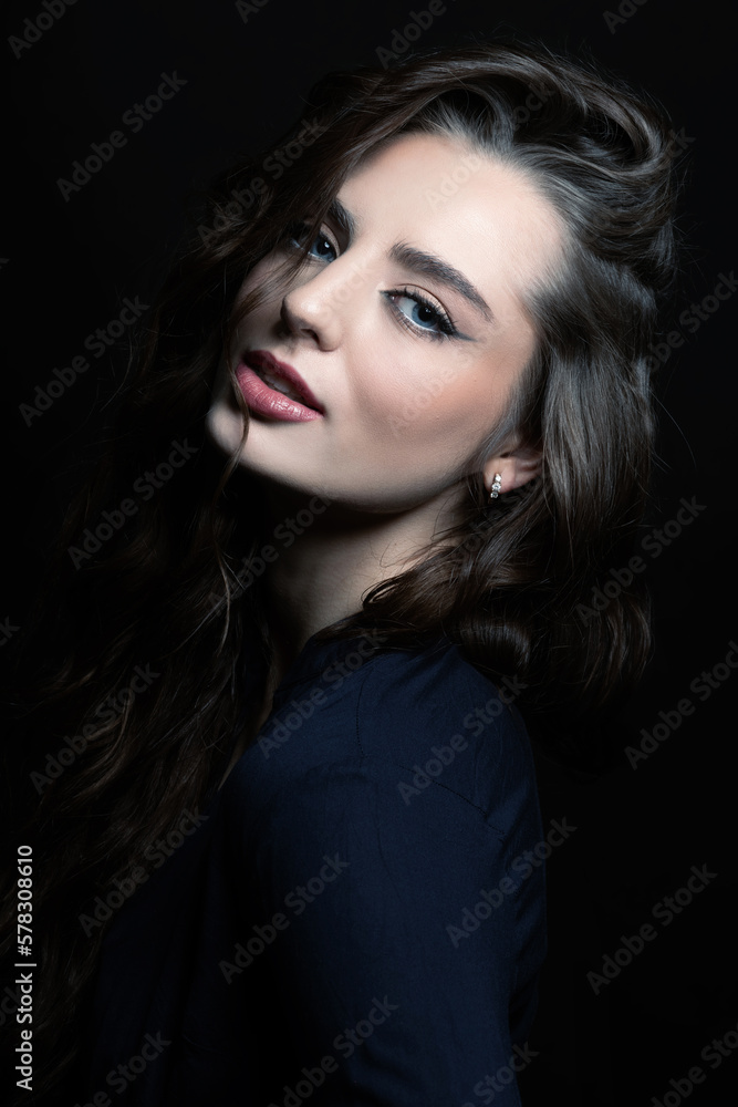 Brunette woman with long wavy hair sensual studio portrait. Model wearing blue blouse and looking at camera with blue eyes and seductive look. Dark studio background. Toned image with blue color Brunette woman with long wavy hair sensual studio portrait. Model wearing blue blouse and looking at camera with blue eyes and seductive look. Dark studio background. Toned image with blue color