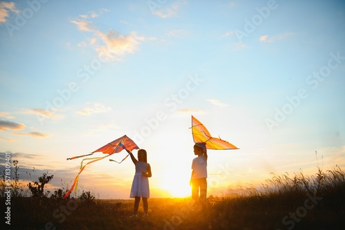 Happy boy and girl playing with kites in field at sunset. Happy childhood concept.
