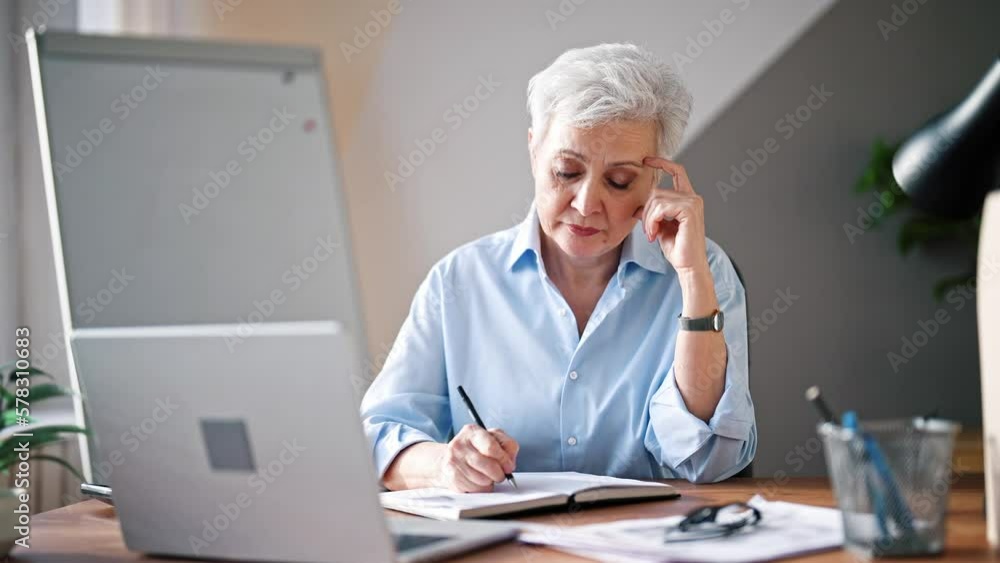 Mature adult european woman at office using laptop computer for work. Beautiful serious professional senior lady. Businesswoman sitting at office table at workplace. Boss office worker. Freelance. Mature adult european woman at office using laptop computer for work. Beautiful serious professional senior lady. Businesswoman sitting at office table at workplace. Boss office worker. Freelance.
