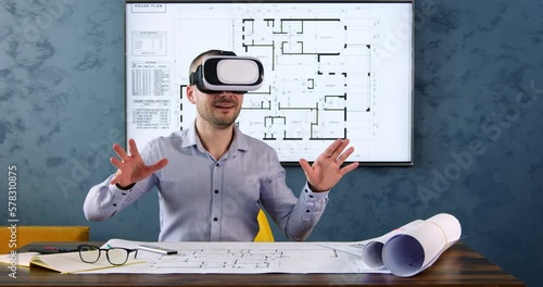 An engineer in 3D glasses gestures with his hands and turns his head, next to it is a paper drawing of a house, in the background there is a screen with a drawing. 3D design of houses. photo