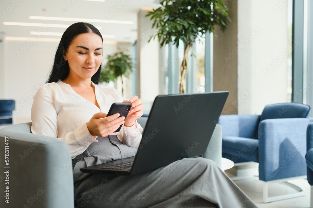 Young business woman sitting at sofa and working with laptop at the waiting hall of the business center Young business woman sitting at sofa and working with laptop at the waiting hall of the business center