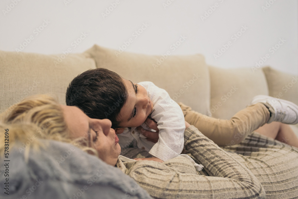 Close-up image of a middle-aged blonde woman lying on the couch holding her young autistic son close to her chest.