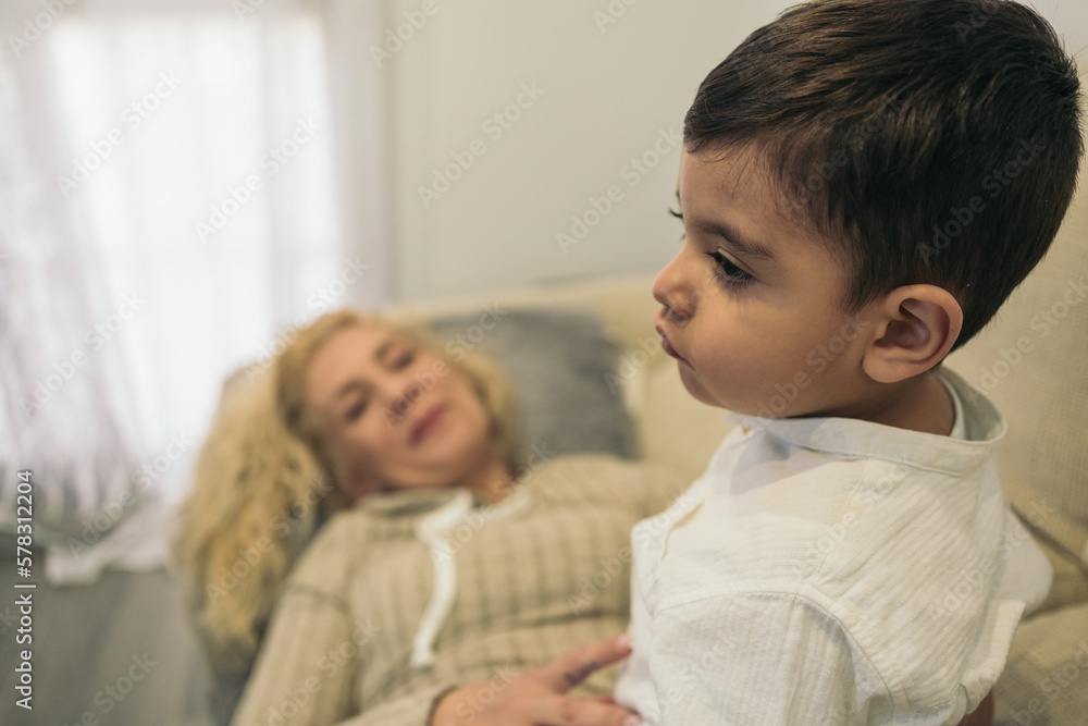 Middle-aged blonde woman lying on the couch smiling and looking intently at her young autistic son sitting on her. Selective focus on the child. Middle-aged blonde woman lying on the couch smiling and looking intently at her young autistic son sitting on her. Selective focus on the child.