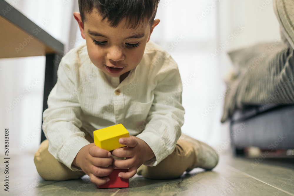 Frontal image of a young autistic child playing at stacking colorful wooden pieces on the living room floor. Frontal image of a young autistic child playing at stacking colorful wooden pieces on the living room floor.