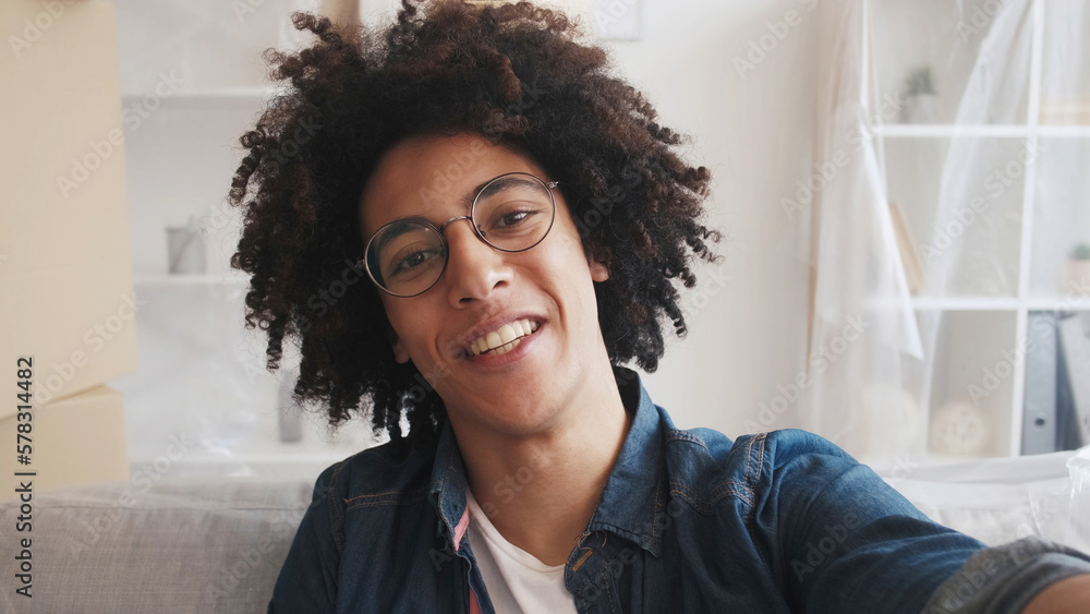 Home selfie. Moving day. Property relocation. Portrait of satisfied happy smiling guy face in glasses taking picture in flat with polyethylene film covered furniture. Home selfie. Moving day. Property relocation. Portrait of satisfied happy smiling guy face in glasses taking picture in flat with polyethylene film covered furniture.
