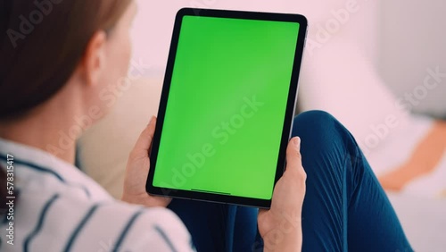 close up woman holding digital tablet vertical scrolling on green screen display sitting on a sofa indoors