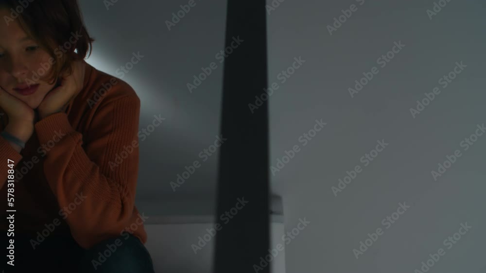 A teenager sits at home with his head resting on his hands, lost in thought under subdued lighting A teenager sits at home with his head resting on his hands, lost in thought under subdued lighting