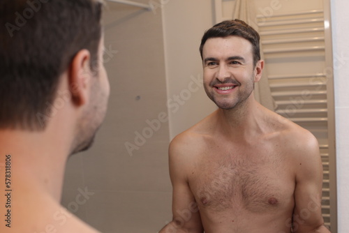 Cute shirtless man looking at his reflection in the bathroom 