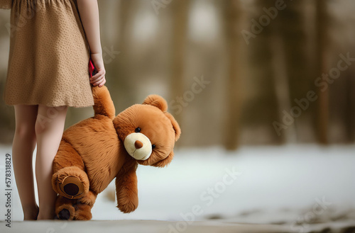 A little girl holds a teddy bear / teddy / stuffed animal in her hand. Background: Snow and forest. The image symbolises sadness, loneliness. Space for text. photo