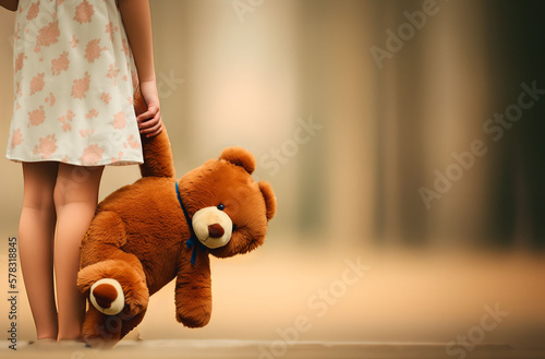 A little girl holds a teddy bear / teddy / stuffed animal in her hand. Background: Light neutral forest. The image symbolises sadness, loneliness. Space for text.