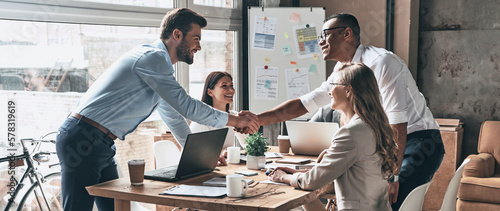 Two young men shaking hands while having meetings with colleagues in the office