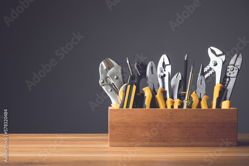 Several yellow tools kit for D.I.Y. in wooden box put on wooden desk with grey wall.