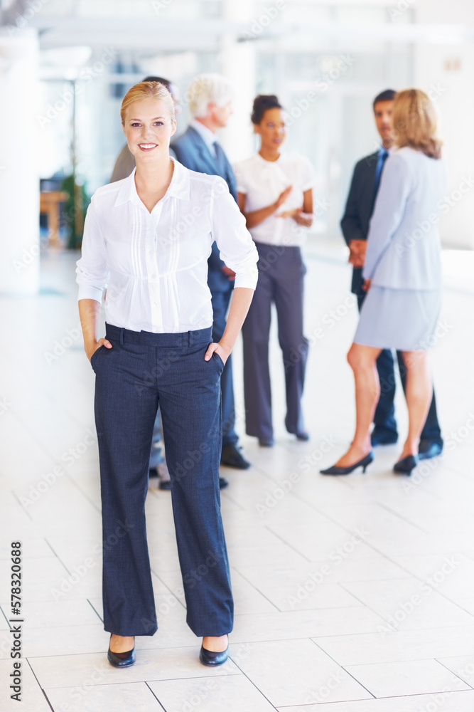 Smiling young executive with business people. Full length of young female executive standing with business people discussing in background. Smiling young executive with business people. Full length of young female executive standing with business people discussing in background.