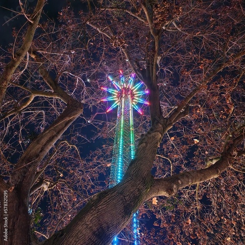 View onto colourful high chairoplane through tree branches at night