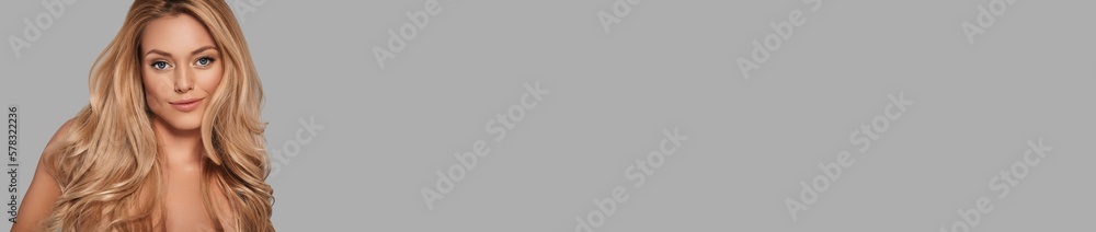 Attractive young woman with long blonde hair looking at camera and smiling against grey background Attractive young woman with long blonde hair looking at camera and smiling against grey background