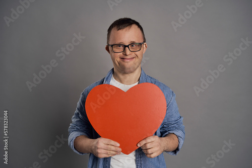 Caucasian man with down syndrome holding big red heart on gray background photo
