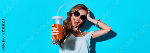 Attractive young woman stretching out hand with cocktail and smiling against blue background