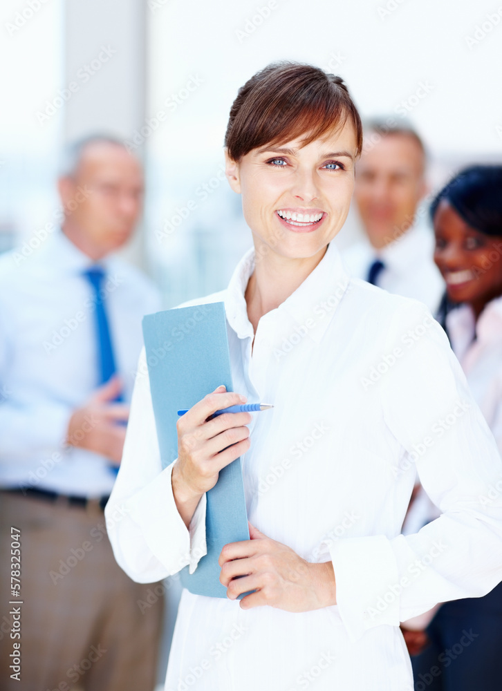 Female executive representing team. Female executive posing with colleagues in background. Female executive representing team. Female executive posing with colleagues in background.