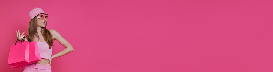 Happy young woman carrying shopping bags while standing against pink background