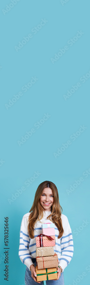 Happy young woman carrying many gift boxes against blue background Happy young woman carrying many gift boxes against blue background