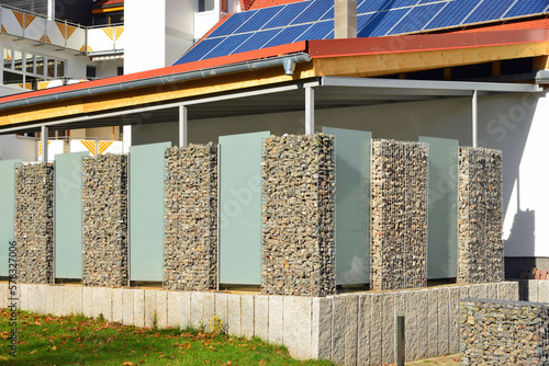 Moderner Sichtschutzzaun abwechselnd aus mit Naturstein gefüllten Gabionen aus verzinktem Stahlgitter und Milchglasplatten um ein bebautes Grundstück mit Wohnhaus und Terrasse photo