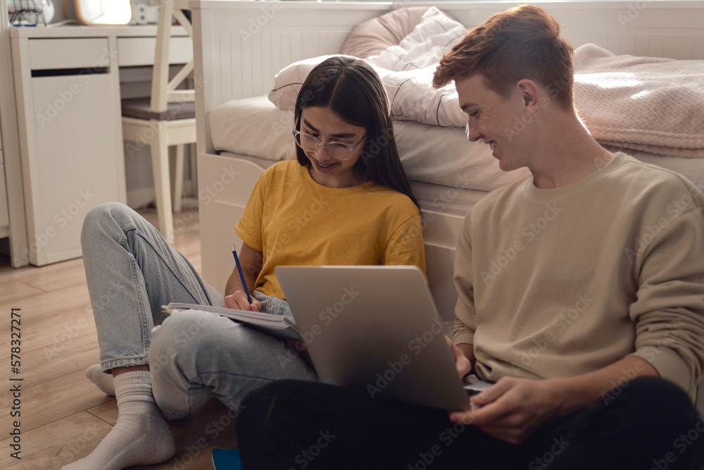 Two caucasian teenagers having fun while sitting on floor and learning from books and laptop Two caucasian teenagers having fun while sitting on floor and learning from books and laptop