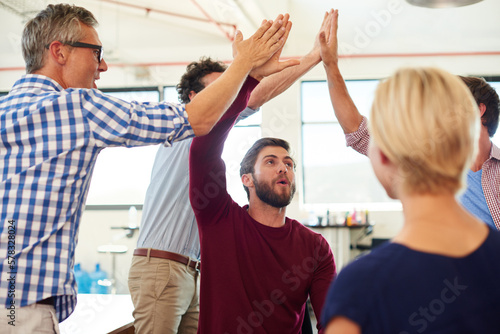 The harder the battle, the sweeter the victory. a group of designer high-fiving each other during an informal meeting.