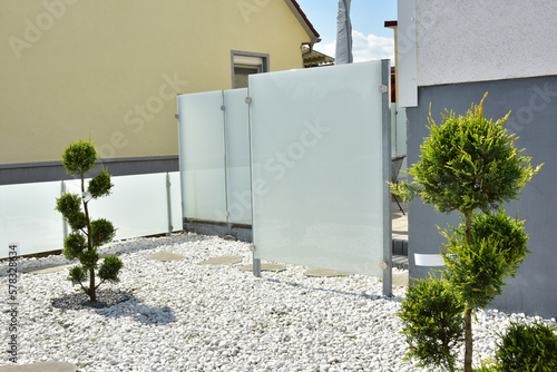 Terrasse und Gartenbereich mit Ziergehölz und Schotterbeet hinter einem Wohnhaus mit Milchglas-Sichtschutz um den Essbereich photo