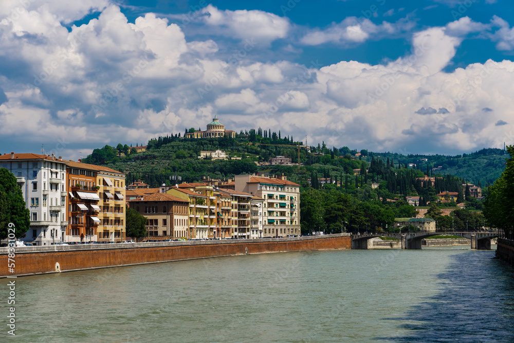 Verona, Italy Adige river view with banks buildings. Day view of hilltop church and sanctuary Madonna di Lourdes.