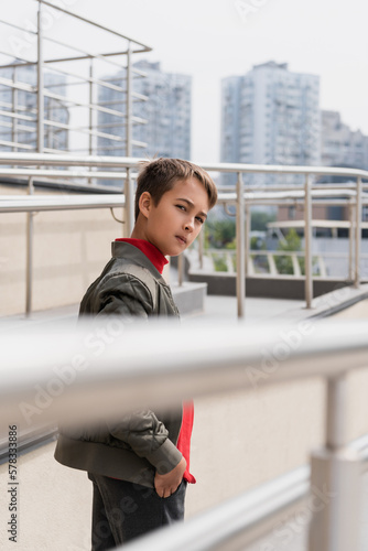 preteen boy in stylish bomber jacket looking at camera near metallic handrails on blurred foreground. © LIGHTFIELD STUDIOS