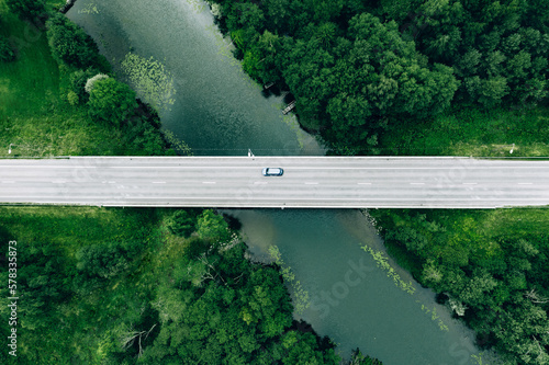 Aerial view of road with blue car over the river and green woods in Finland