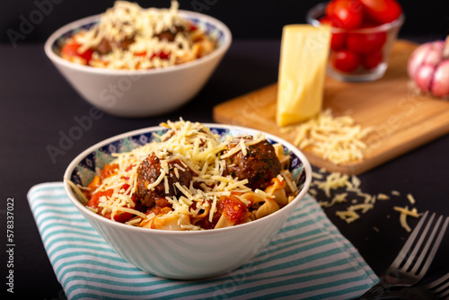 Classic italian tagliatelle spaghetti pasta with tomato sauce, meatballs, parmesan cheese and basil in plate on dark table. Dark food, dark mood