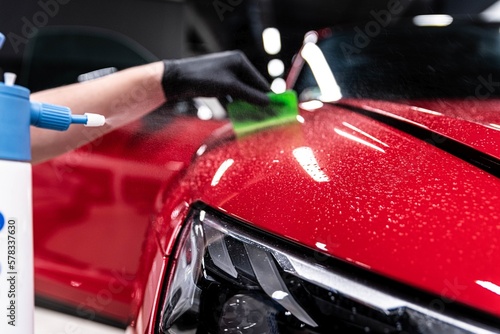 Application of a colorless protective film at a car detailing studio or car wash. Beautiful red car paint.