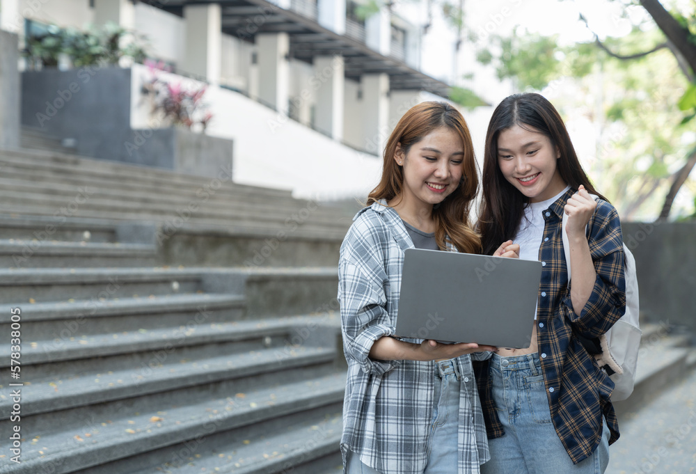 Asian female college students look at and study insights and biology on a laptop and record in a notebook at the outside university. Asian female college students look at and study insights and biology on a laptop and record in a notebook at the outside university.
