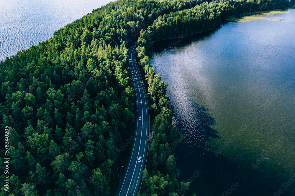 Aerial view of road in green woods and blue lakes water in Finland