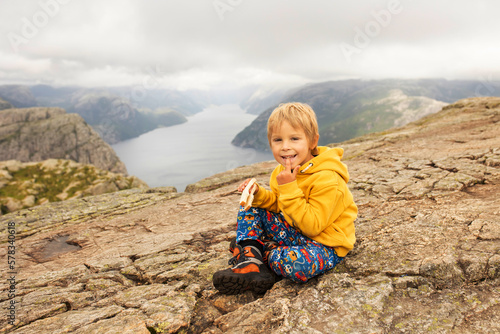 Family, enjoying the hike to Preikestolen, the Pulpit Rock in Lysebotn, Norway on a rainy day, toddler climbing with his pet dog the one of the most scenic fjords