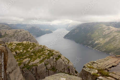 Family, enjoying the hike to Preikestolen, the Pulpit Rock in Lysebotn, Norway on a rainy day, toddler climbing with his pet dog the one of the most scenic fjords