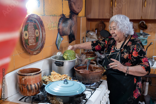 A senior mexican woman is smiling while preparing chayote to go with battered poblano chiles