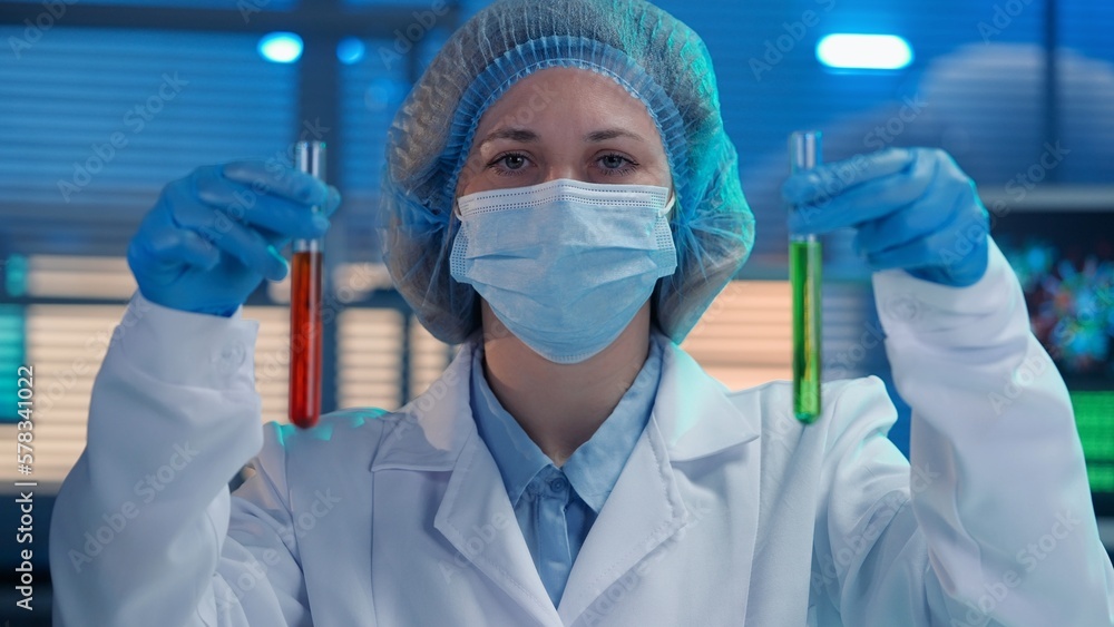 A woman scientist holds test tubes with red and green liquid in her hands. Portrait of a woman in blue gloves, a white medical gown, bonnet and a mask. Research in a modern biochemical laboratory. A woman scientist holds test tubes with red and green liquid in her hands. Portrait of a woman in blue gloves, a white medical gown, bonnet and a mask. Research in a modern biochemical laboratory.