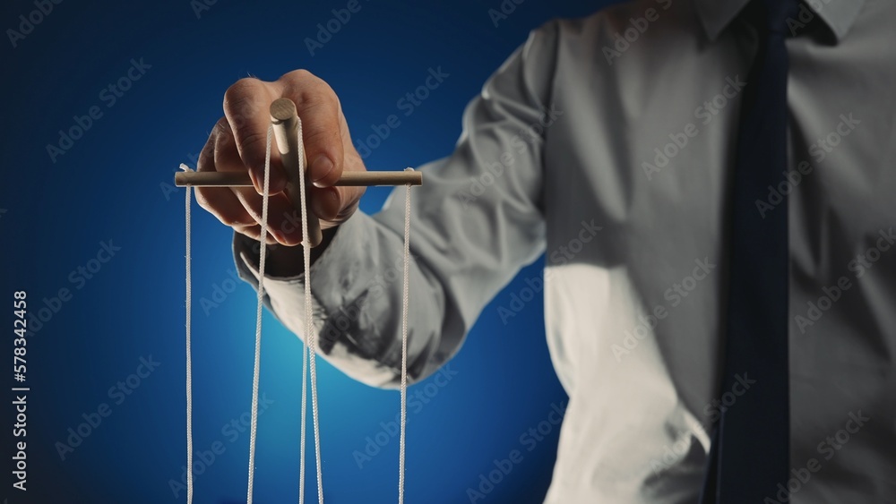 A businessman in a gray shirt and black tie controls a puppet with a