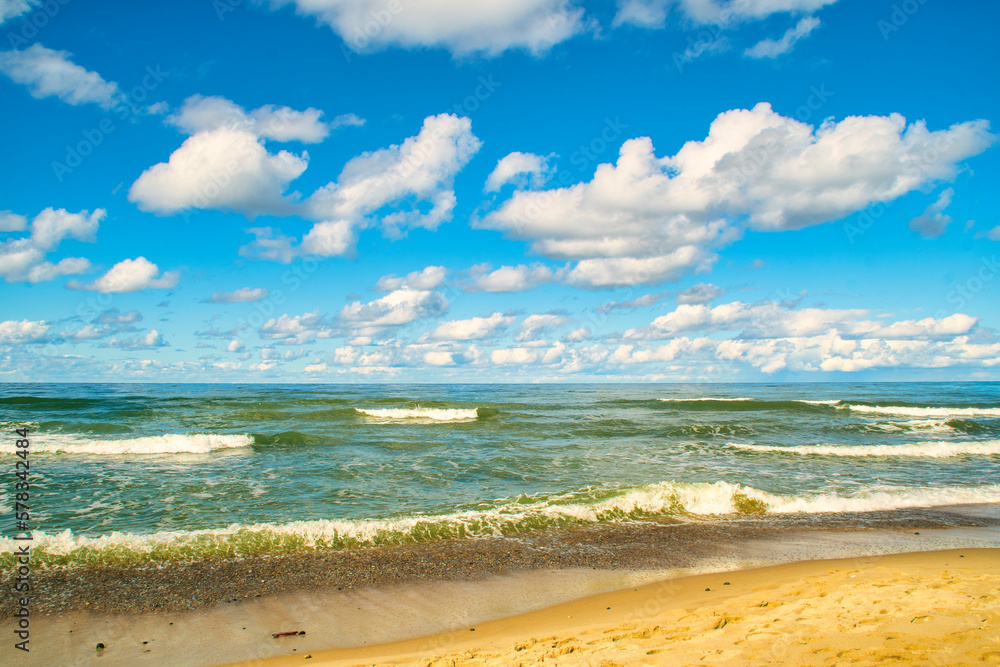 A sandy seashore with clouds. Background with the sky and the surf on the theme of beach holidays and sea travel.