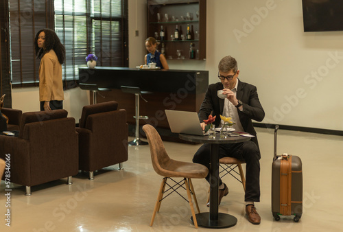 A male traveler enjoys a cup of coffee while using airline business lounge at a terminal waiting for departure. Business man uses computer laptop to check his travel plan and boarding in a lobby room.