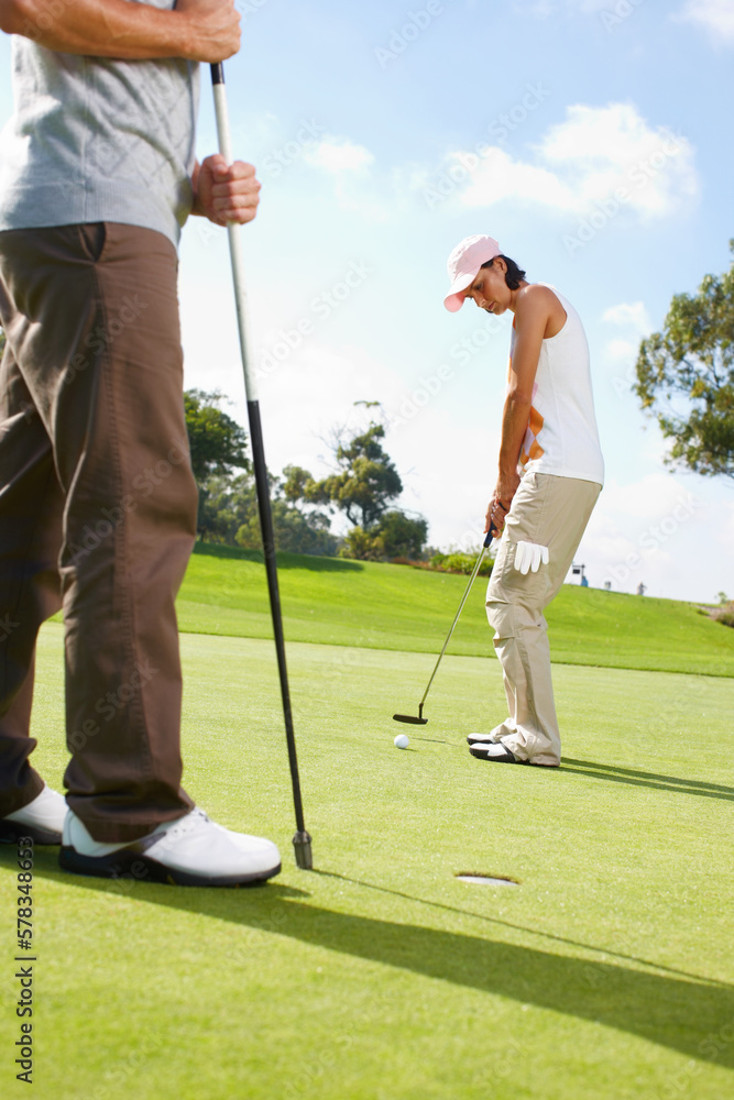 Obraz premium She doesnt let anything distract her. Young woman putting on the golf course with her husband in the background.