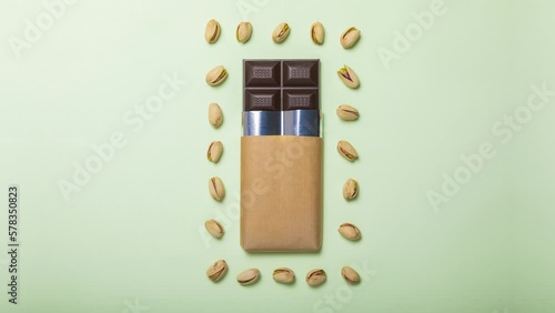 Mockup of a delicious handmade dark chocolate bar, on green background, surrounded by dancing and moving pistachio nuts