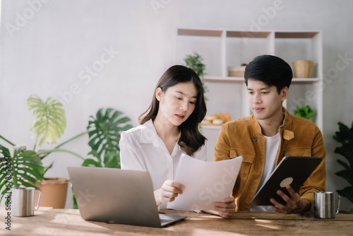 Photo of cute cheerful young couple using laptop and analyzing their finances with documents.