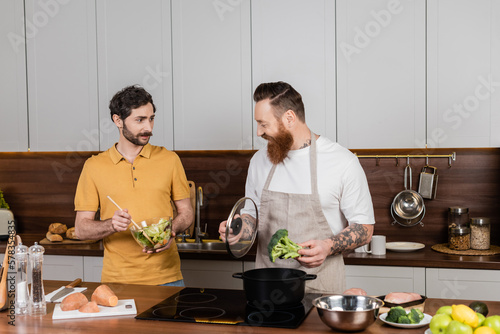 Same sex family cooking vegetables and making salad together in kitchen.